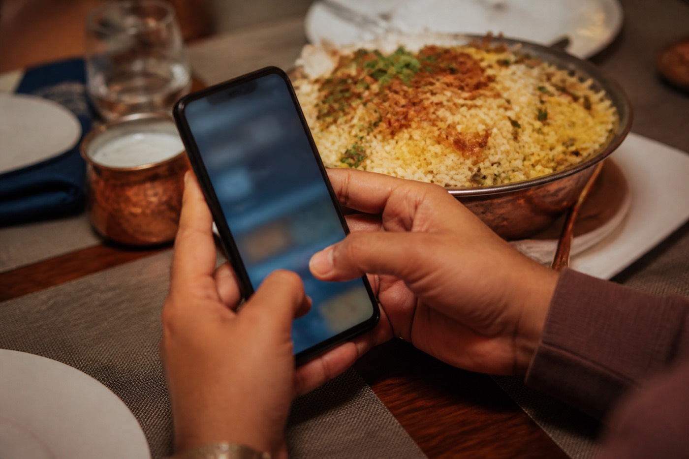 A guest at the table with a phone, biryani in the background.